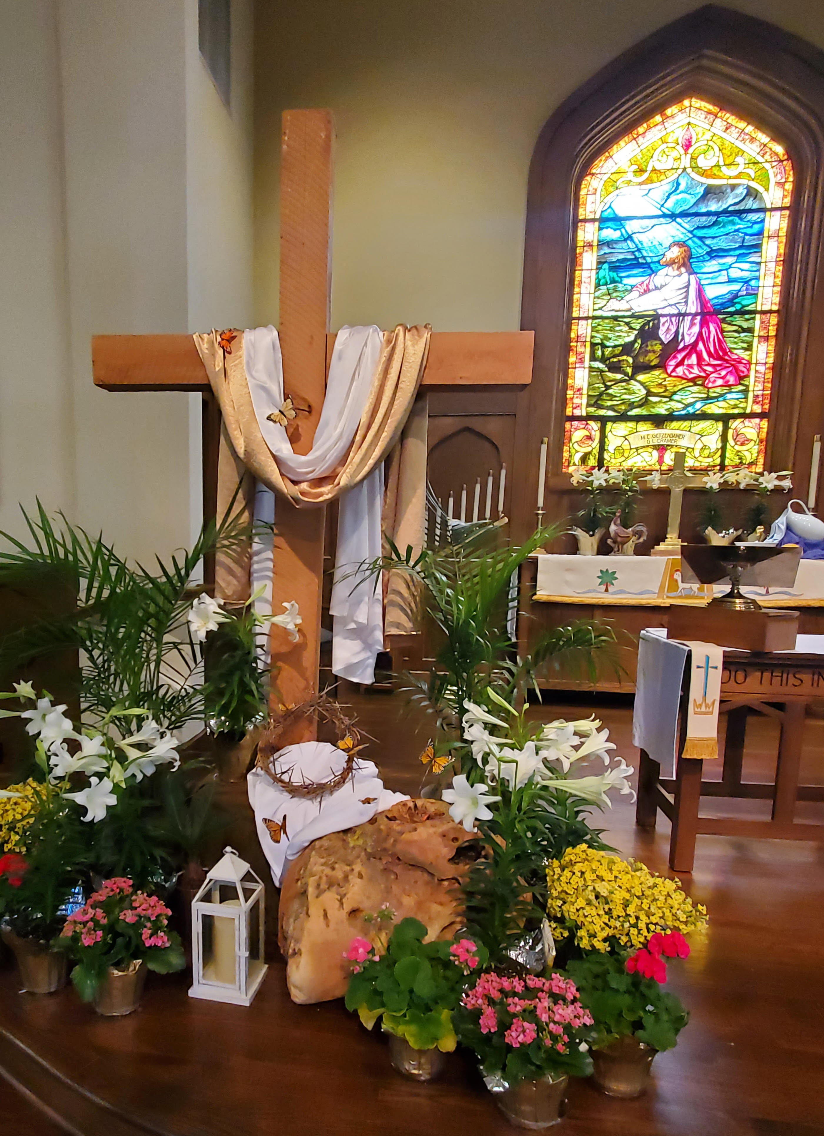 St. Mark Lutheran Church Sanctuary decorated with Easter lilies, a wooden cross draped with white and gold fabric, and a beautiful stained glass window